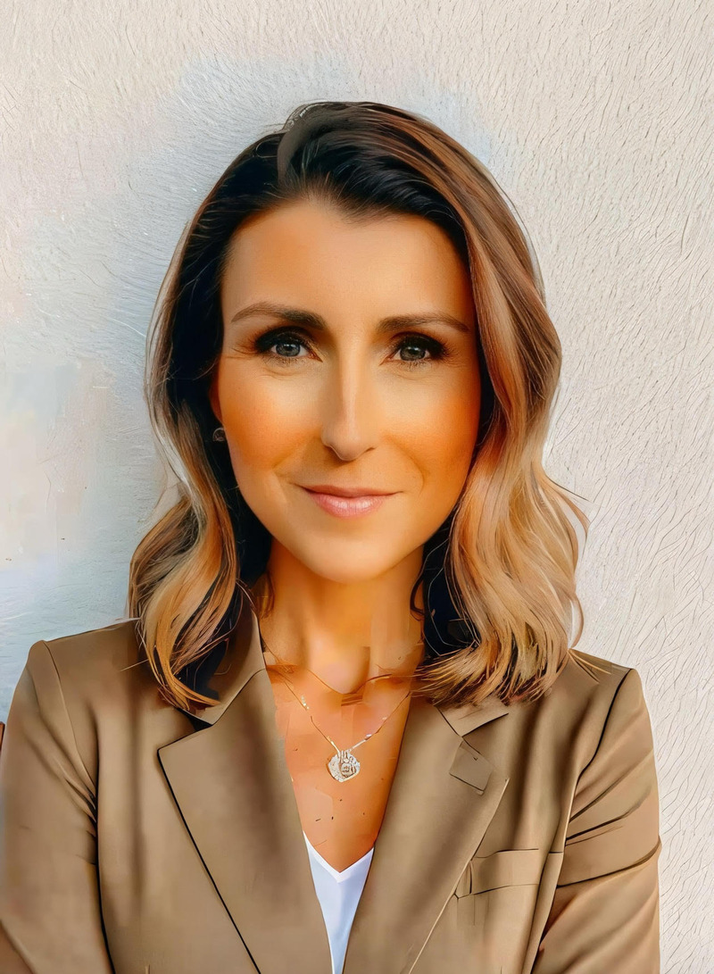 Woman in tan suit and diamond necklace confidently smiling at the camera